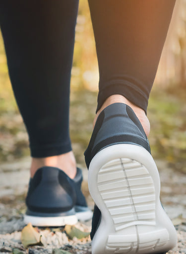A person wearing KSNS shoes seen from behind, strolling down a park path.